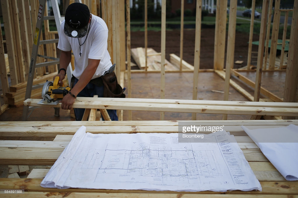 A set of blueprints sit in front of a contractor cutting lumber for a house under construction in the Norton Commons subdivision of Louisville, Kentucky, U.S., on Friday, July 29, 2016. The U.S. Census Bureau is scheduled to release construction spending figures on August 1. Photographer: Luke Sharrett/Bloomberg